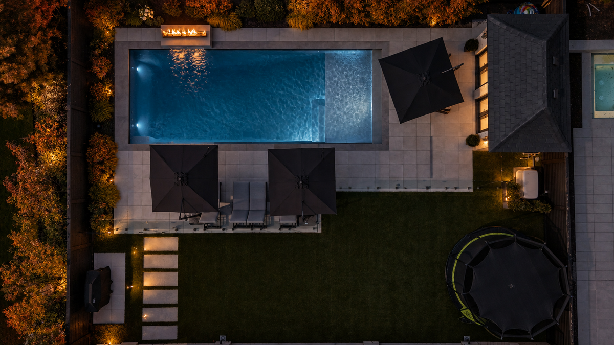 Overhead view of a Betz backyard pool at night, with dark water, autumn foliage and warm firelight.